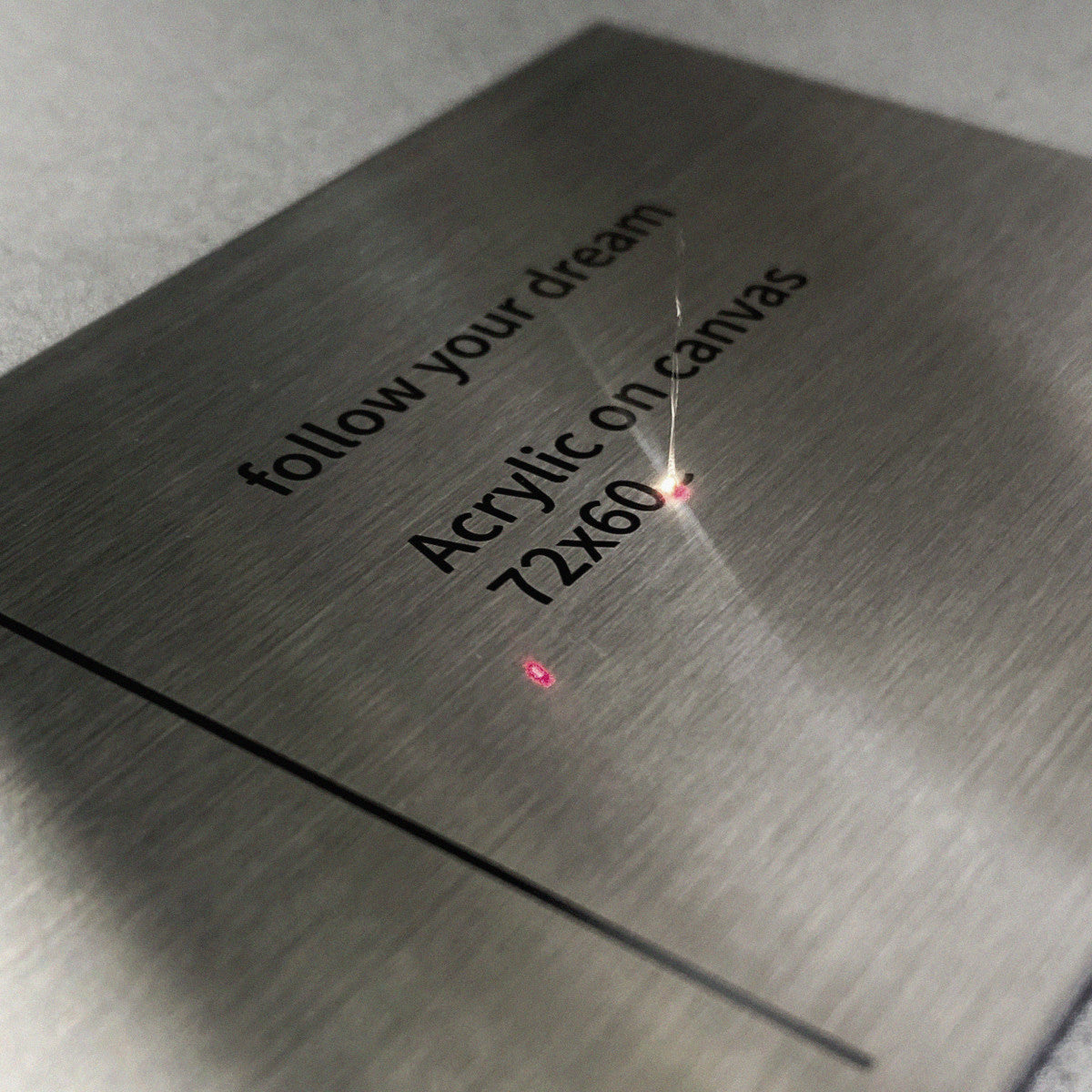 Laser engraving process in progress on brushed stainless steel surface, with precision-guided red beams etching customized typography.